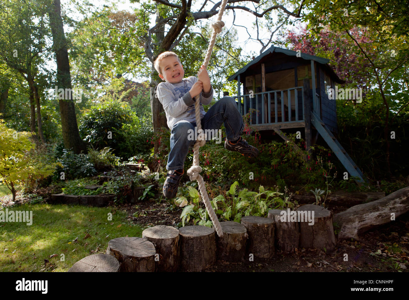 Boy playing on rope swing in backyard Stock Photo