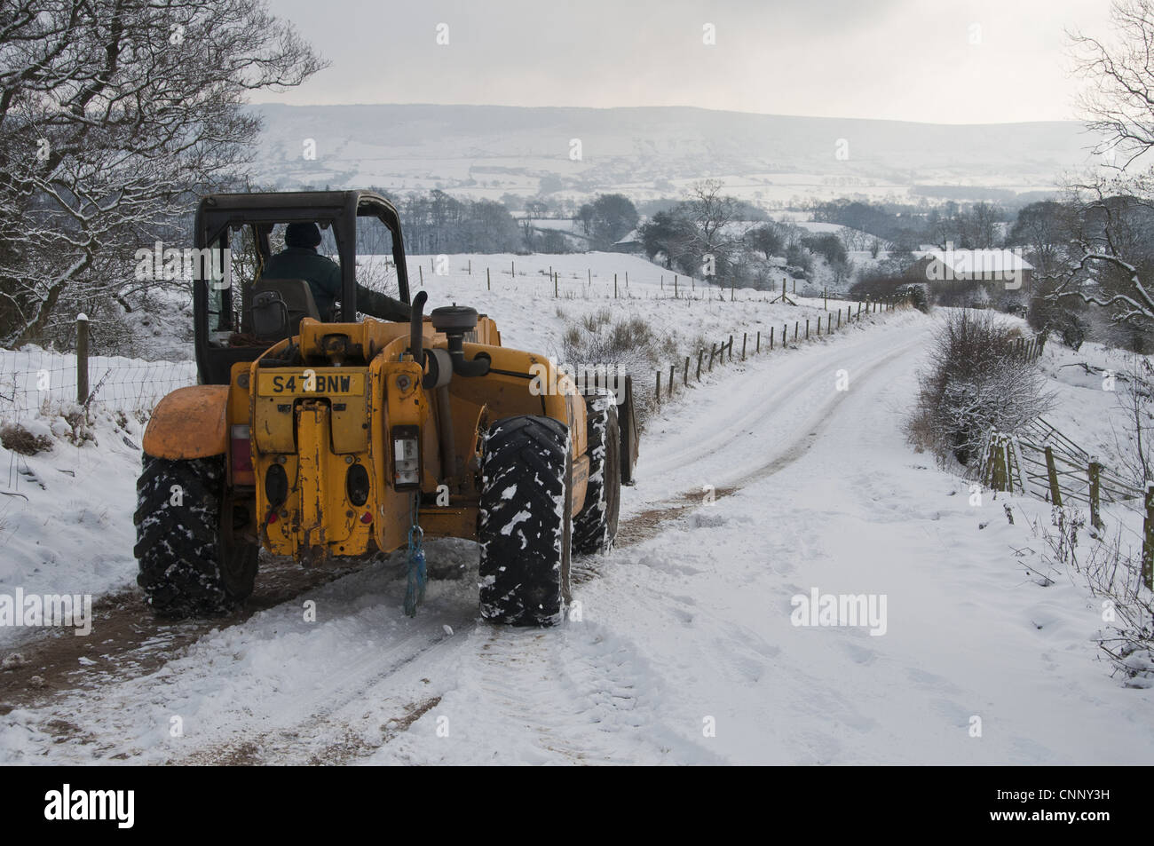 JCB 530 loader clearing snow from road for milk tanker on dairy farm, Whitewell, Lancashire, England, december Stock Photo