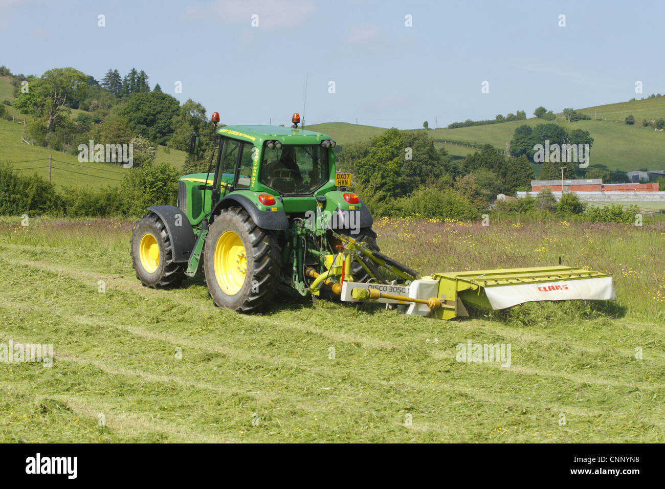 Contractor with John Deere tractor and Claas mower, cutting grass for