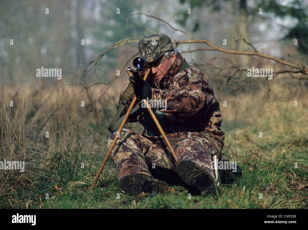 Hunting, deer stalker sitting on low seat and using tripod to support rifle, England Stock Photo