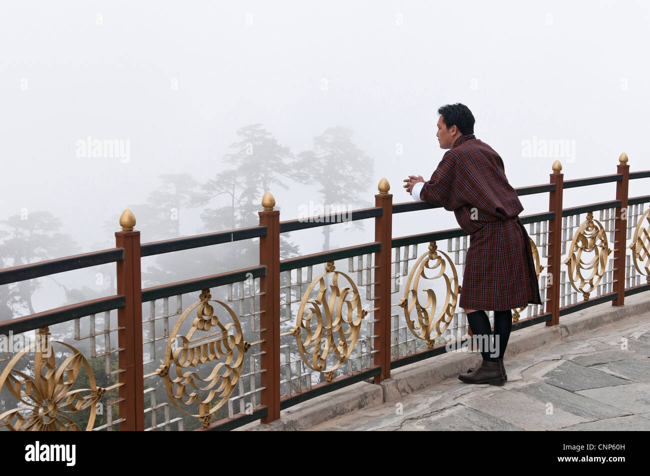 Asia, Bhutan, Dochu La. Man wearing traditional Gho garb looking into fog-shrouded trees Stock Photo