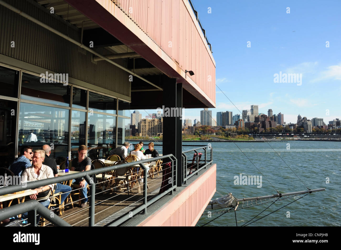 BLue sky view people sitting talking, Harbour Lights Restaurant, to Brooklyn skyline, Pier 17, South Street Seaport, New York Stock Photo
