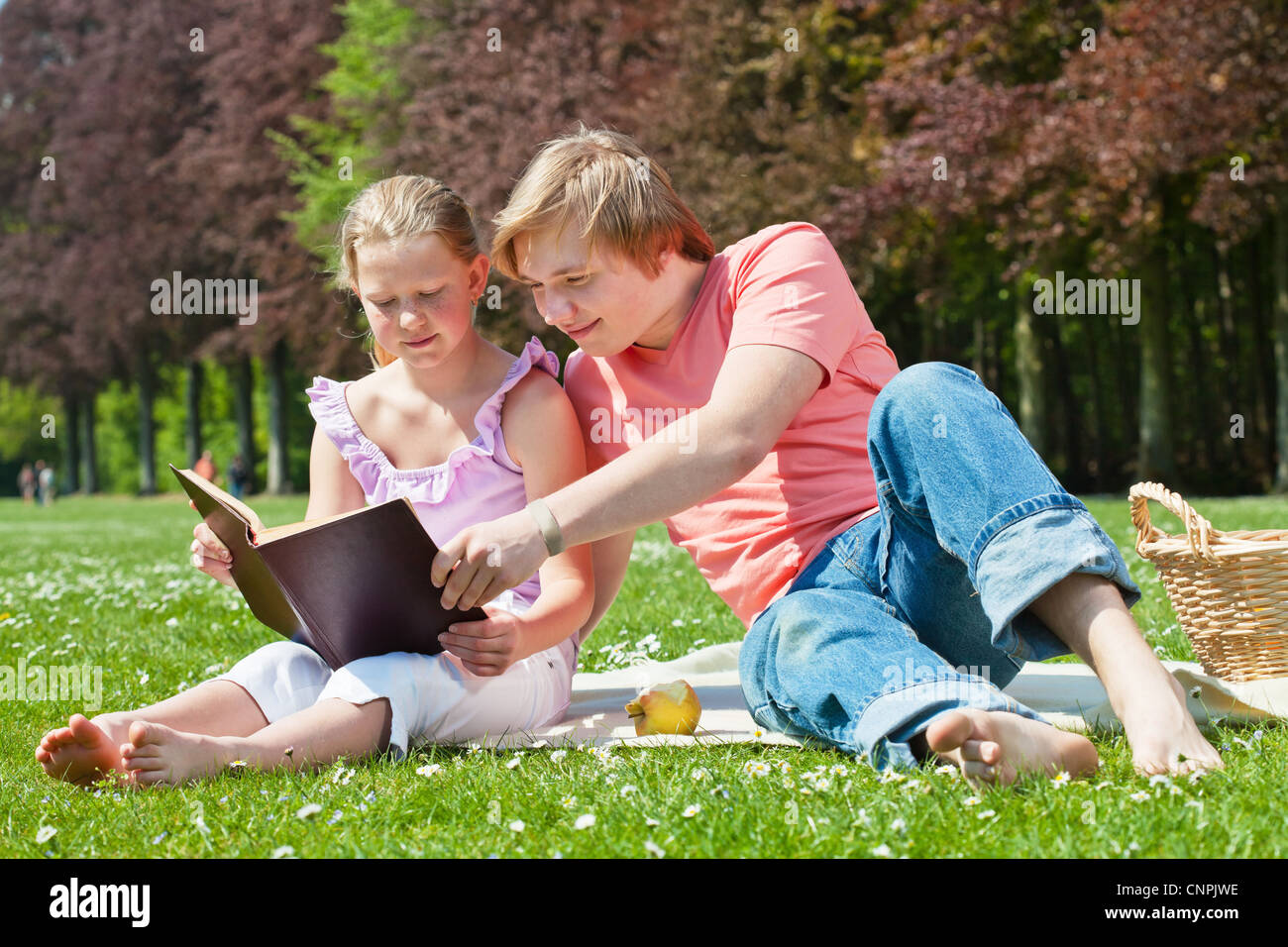 Teenager siblings reading book at picnic in the park in a bright sunny day Stock Photo