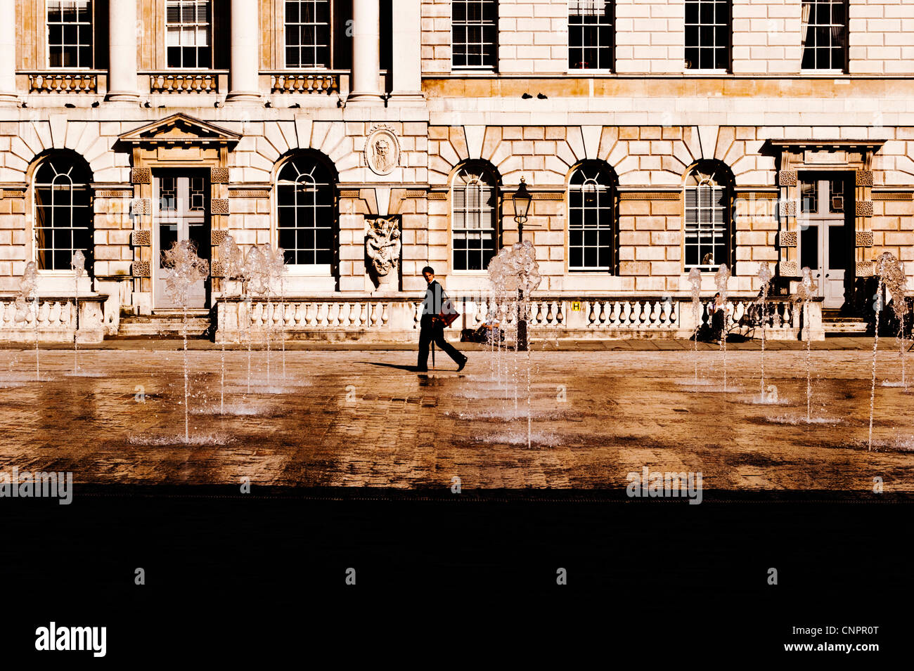 Man walking past the fountains at Somerset House, London, England, UK Stock Photo