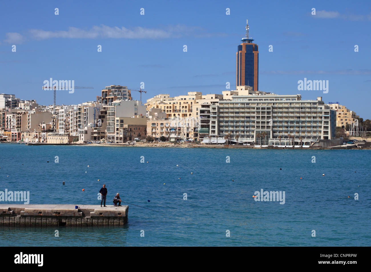 Two men fishing at St Julians with Hotel Cavalieris and high rise Portomaso tower  in the background Malta, Europe Stock Photo