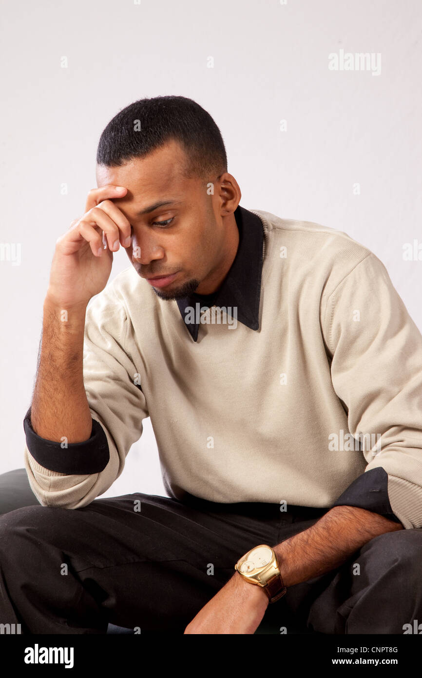 Young black man in brown sweater, sitting with hand on forehead, thinking serious thoughts Stock Photo