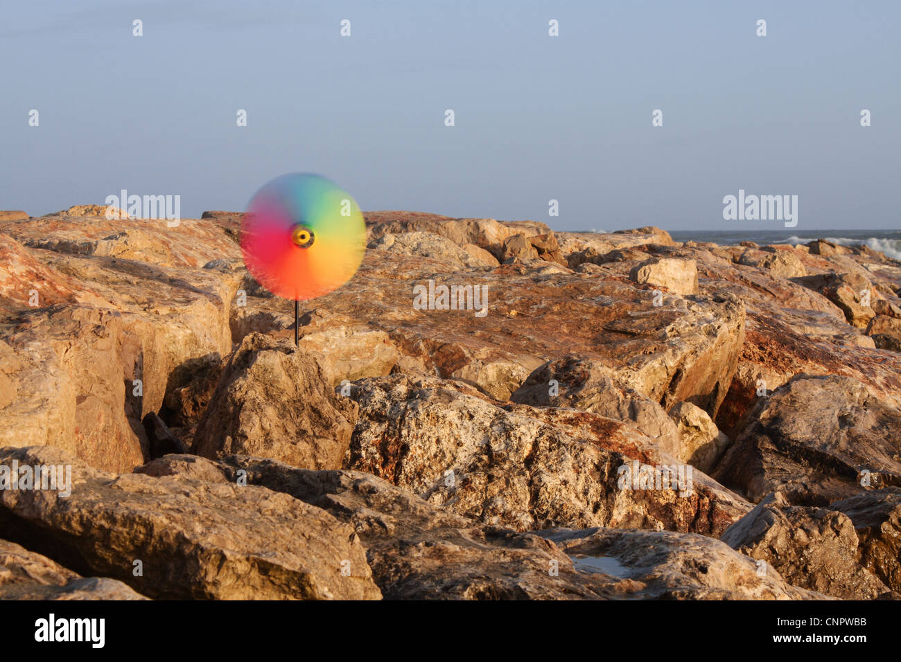 A colorful pinwheel turns with the energy of the wind in a seascape scenario in the golden hour. Stock Photo