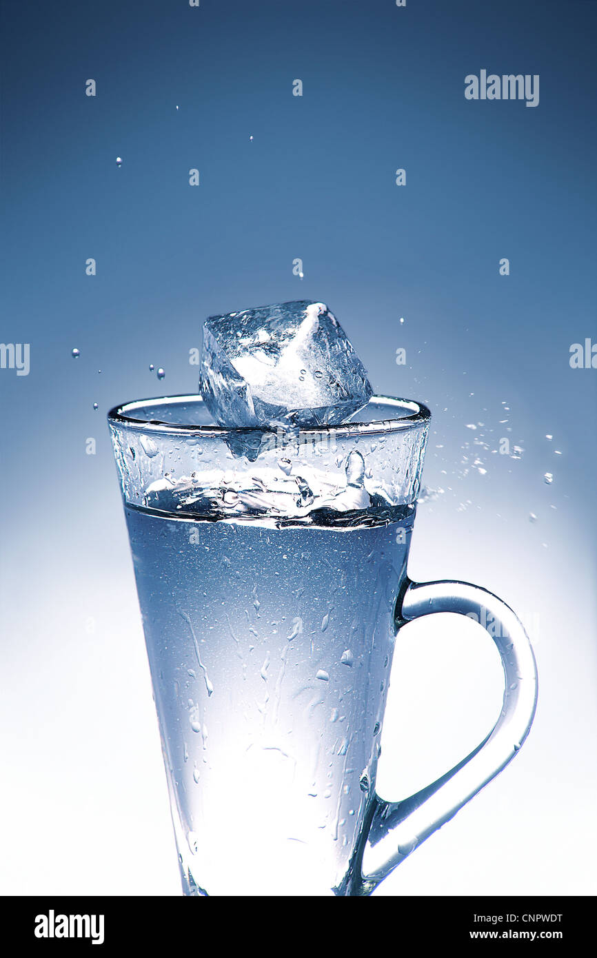 Ice cube splashing into glass of water Stock Photo - Alamy