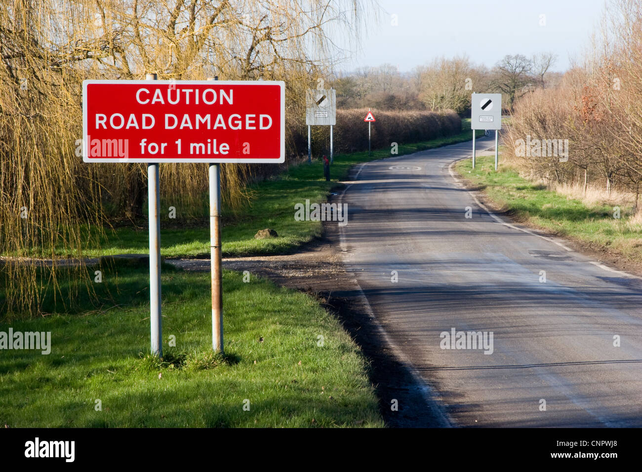 Country road between Hannington and Kempsford with sign stating, 'CAUTION ROAD DAMAGED for 1 mile' Stock Photo