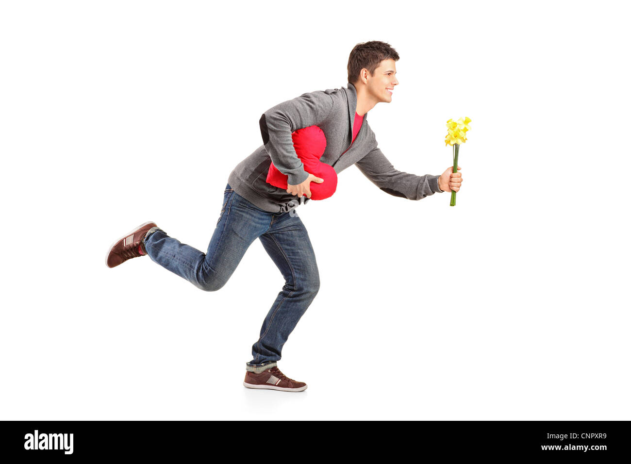 Young man running with a bunch of flowers and red heart shape object in his hands isolated on white background Stock Photo