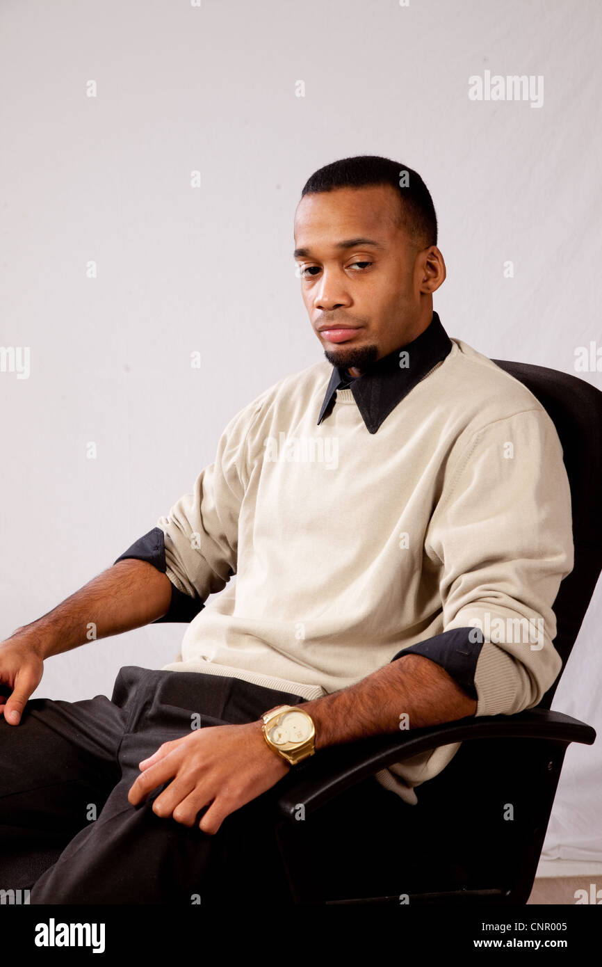 Thoughtful young black man, wearing sweater and looking all pensive and sad  sitting in an executive's chair Stock Photo