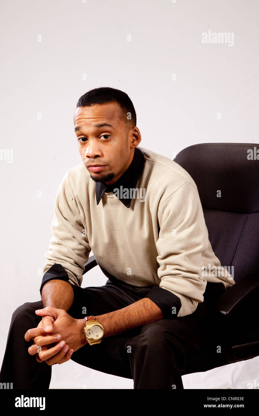 Thoughtful young black man, wearing sweater and looking all pensive and sad  sitting in an executive's chair leaning forward Stock Photo