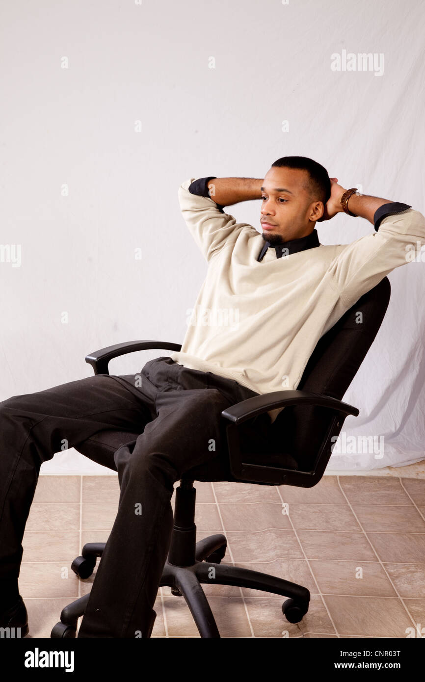 Thoughtful young black man, wearing sweater and looking all pensive and sad  sitting in an executive's chair leaning back Stock Photo