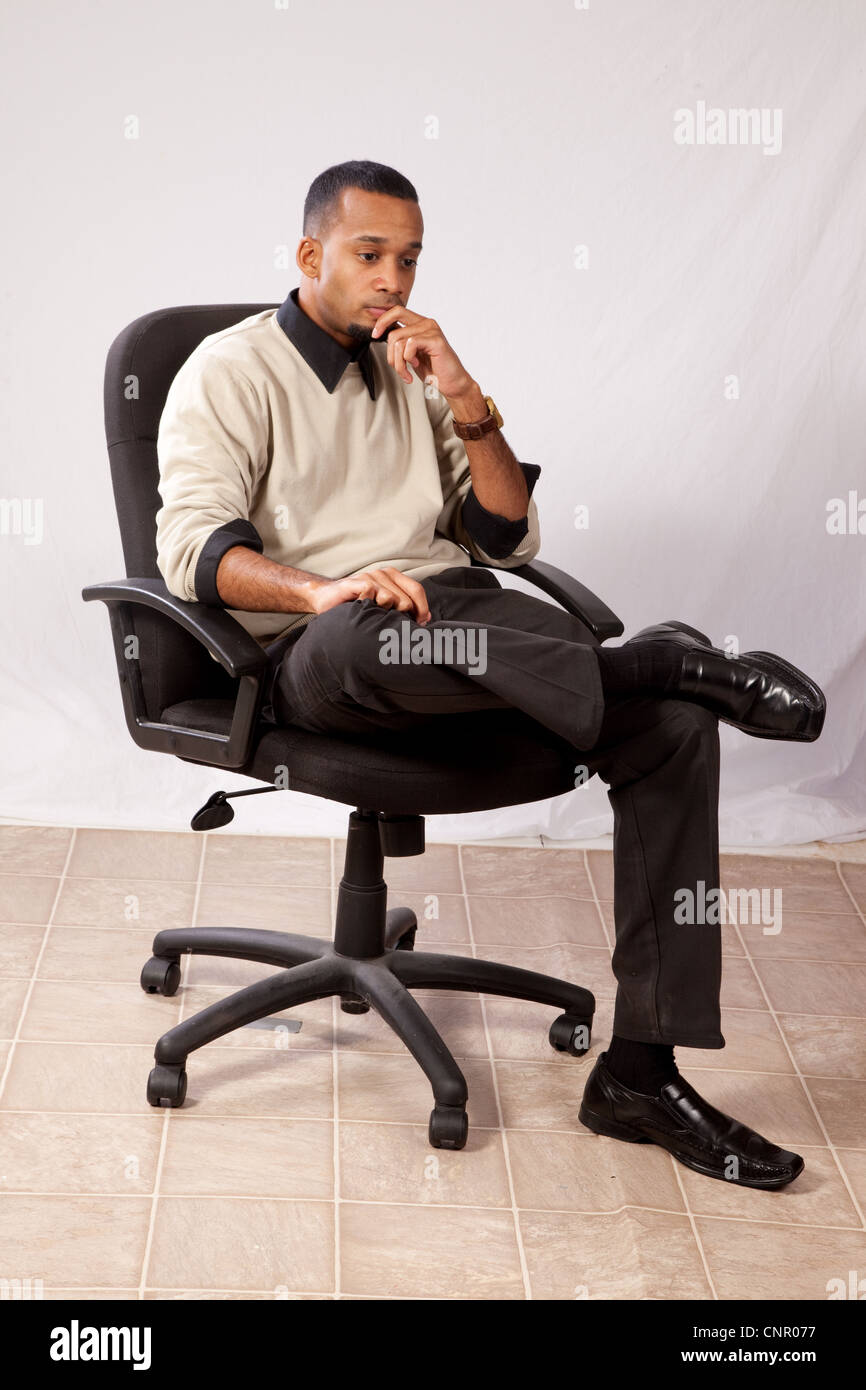 Thoughtful young black man, wearing sweater and looking all pensive and sad  sitting in an executive's chair Stock Photo