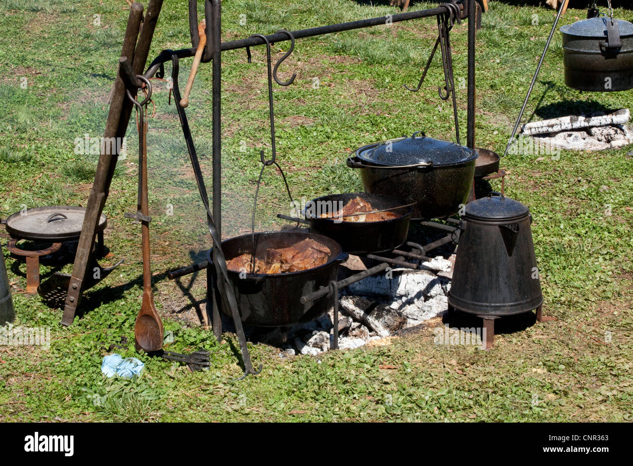 Cooking over a camp fire, with cast iron pots and coffee pot, outdoors in  the sunshine Stock Photo - Alamy