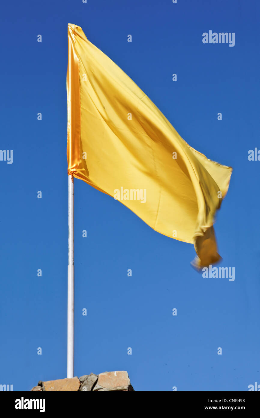 Vertical portrait of silky yellow flag flying high aginst a deep blue sky Stock Photo