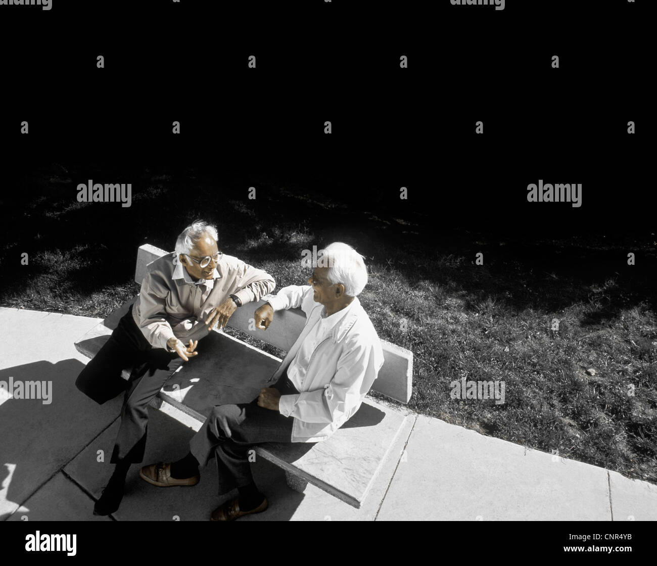two elderly ethnic men sitting on a bench talking Stock Photo