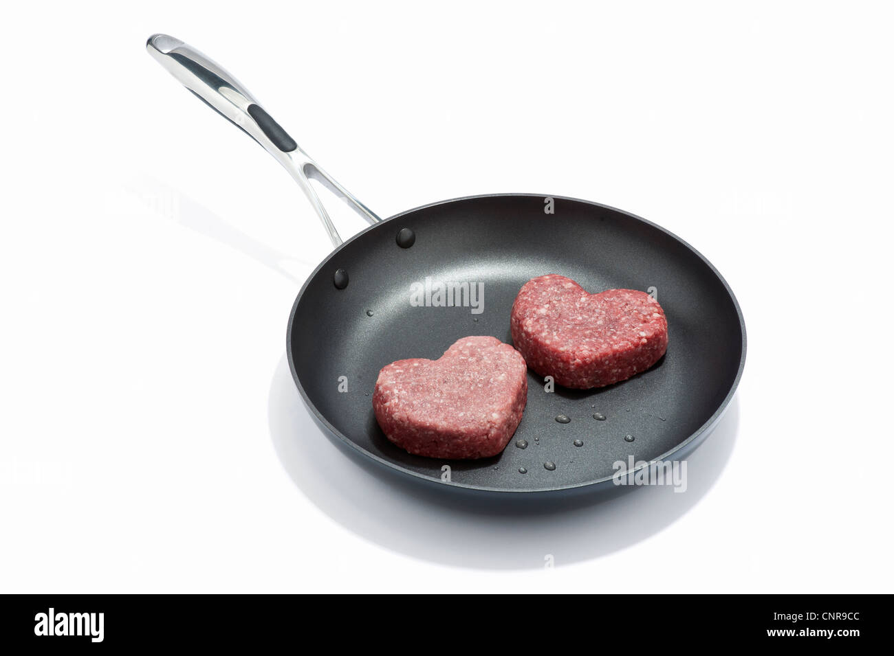 Two heart shaped beef burgers in a frying pan Stock Photo