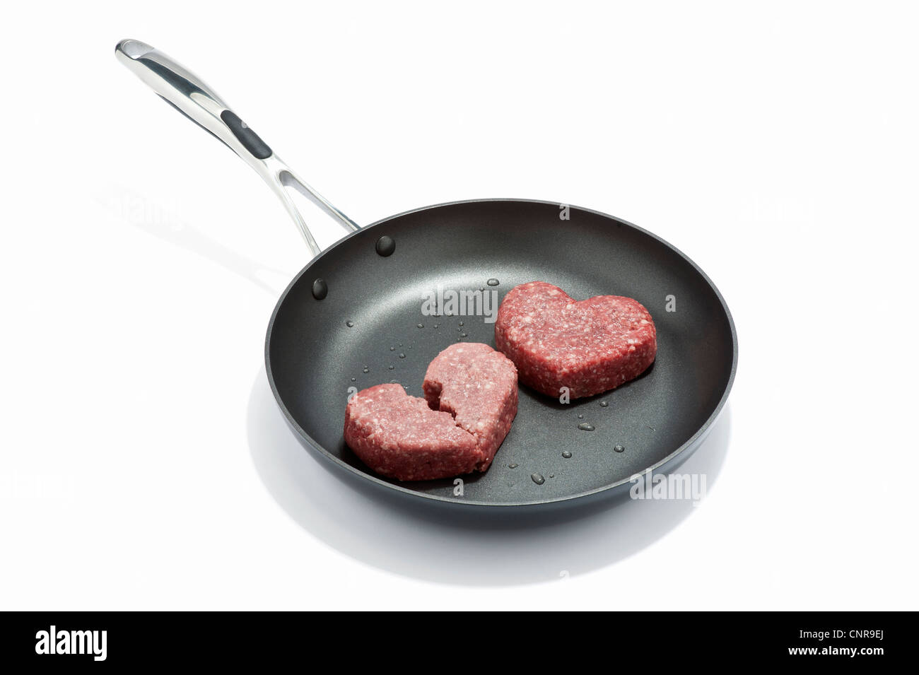 Two heart shaped beef burgers in a frying pan Stock Photo