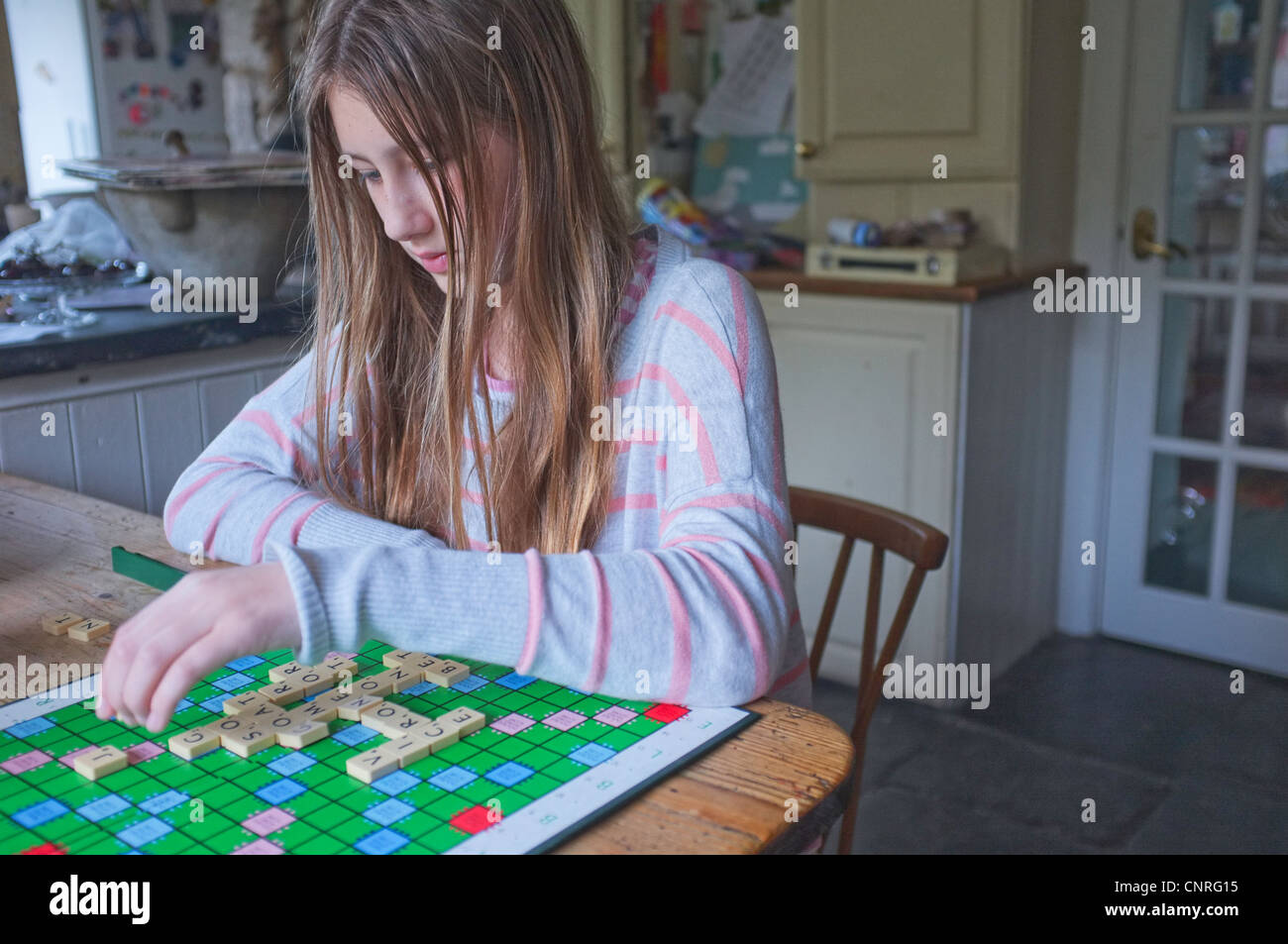 An 11 year old girl playing Scrabble in a kitchen Stock Photo