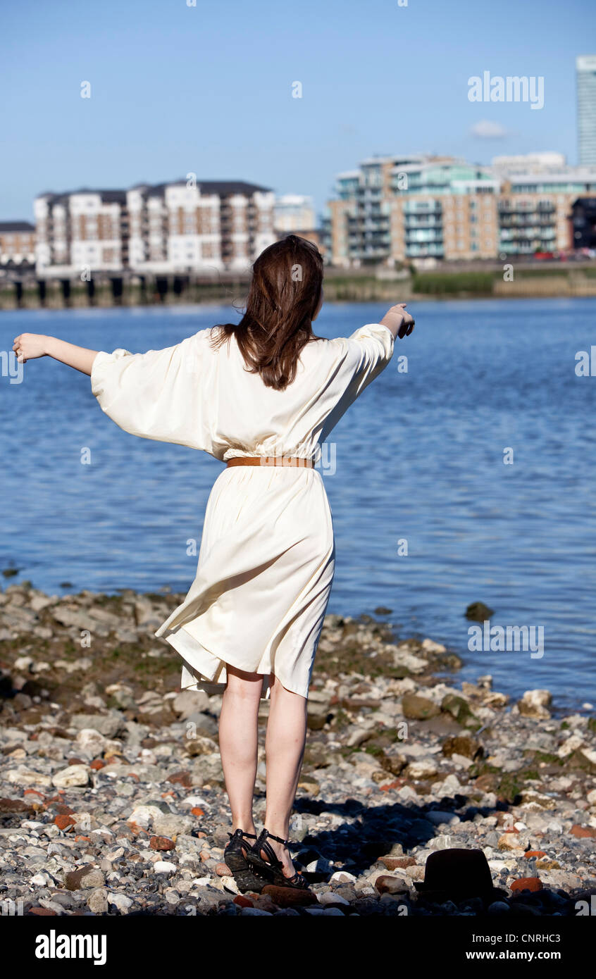 Rear view, full length portrait of a woman standing at a shore pointing out into the distance, London, England, UK Stock Photo