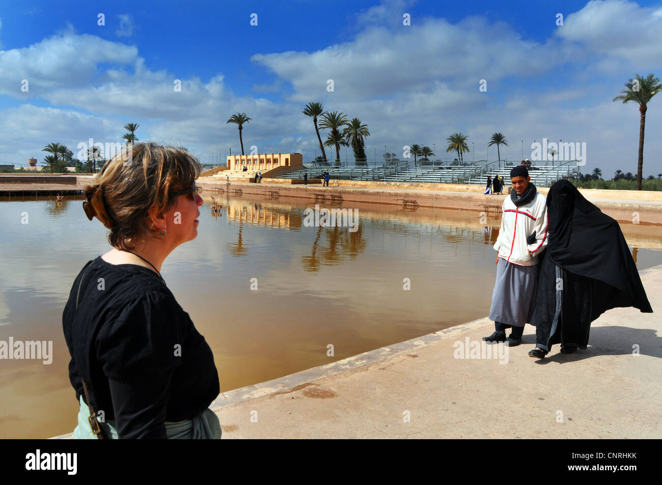 Western tourist walks past Muslim couple in full hijab, Menera Gardens, Marrakesh Morocco North Africa Stock Photo