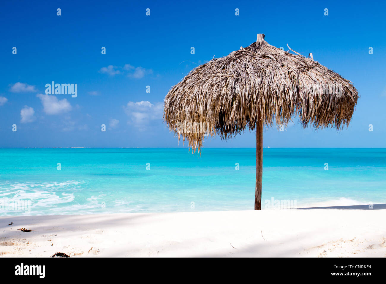 Beach Umbrella made of palm leafs on a perfect white beach in front of Sea. The right place for relax and vacations Stock Photo
