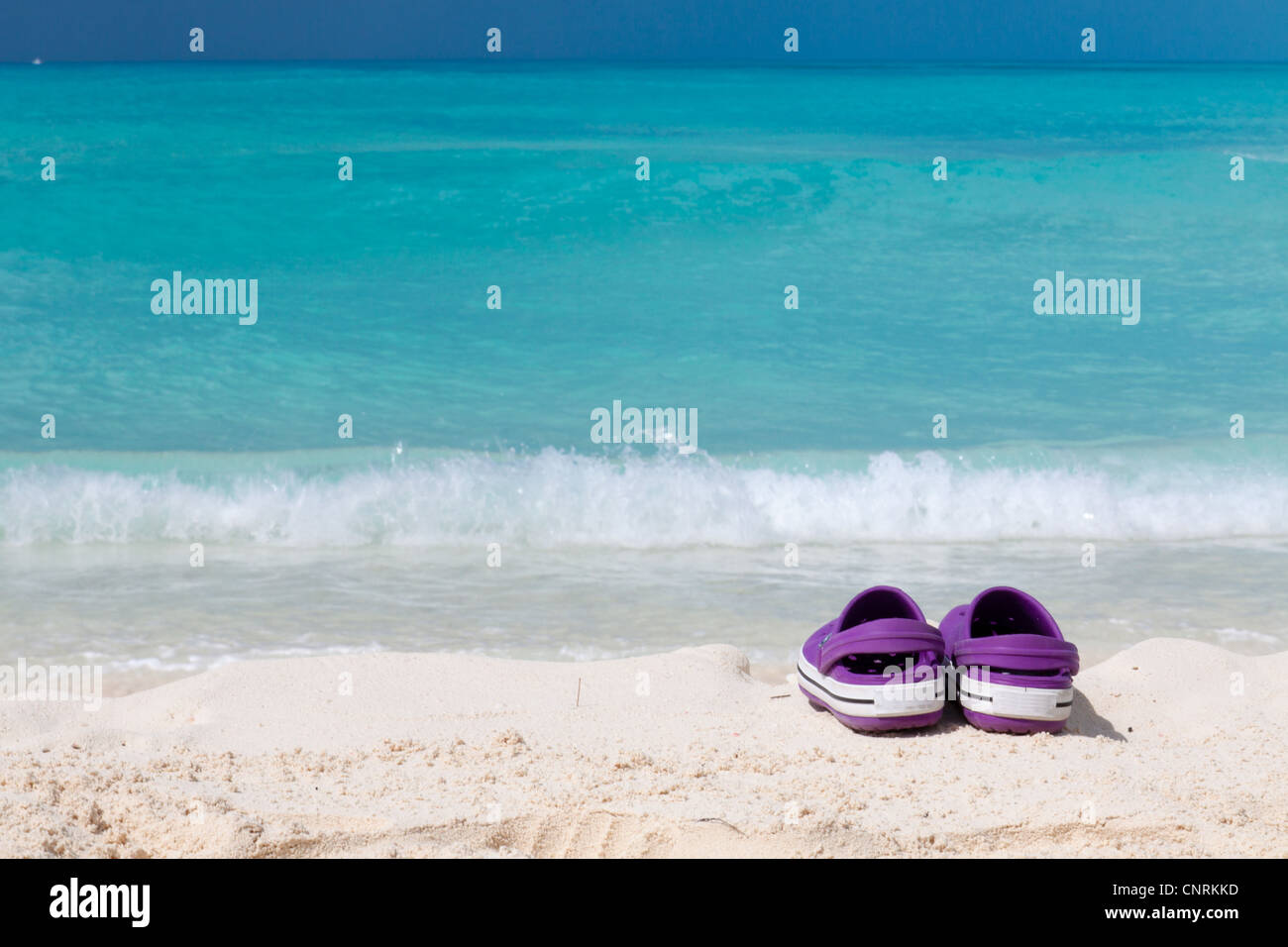 Pair of colored sandals on a white sand beach in front of the sea. The right place for relaxation and vacations Stock Photo