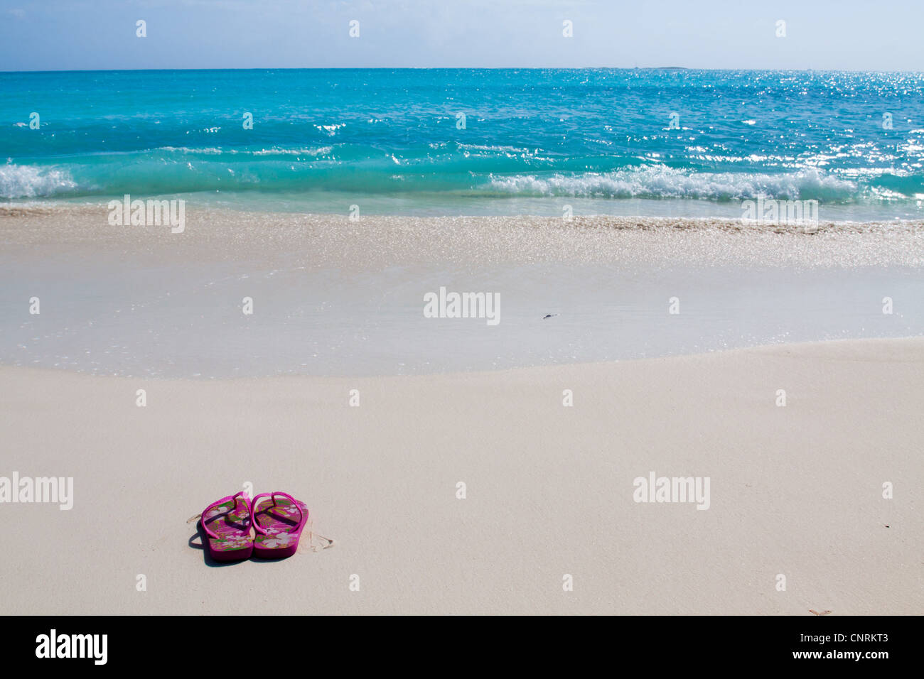 Pair of colored sandals on a white sand beach in front of the sea. The right place for relaxation and vacations Stock Photo