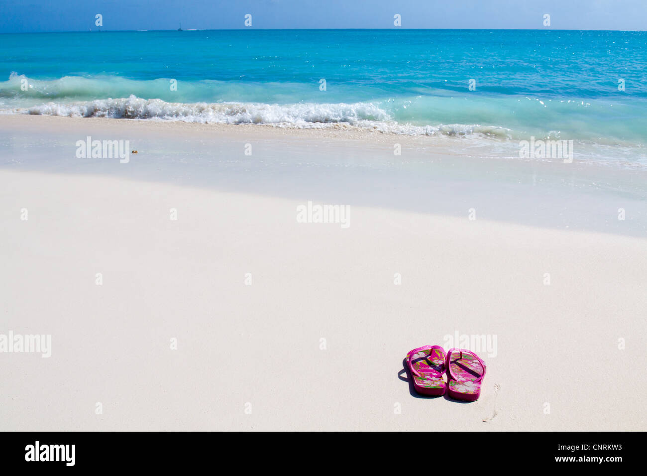 Pair of colored sandals on a white sand beach in front of the sea. The right place for relaxation and vacations Stock Photo