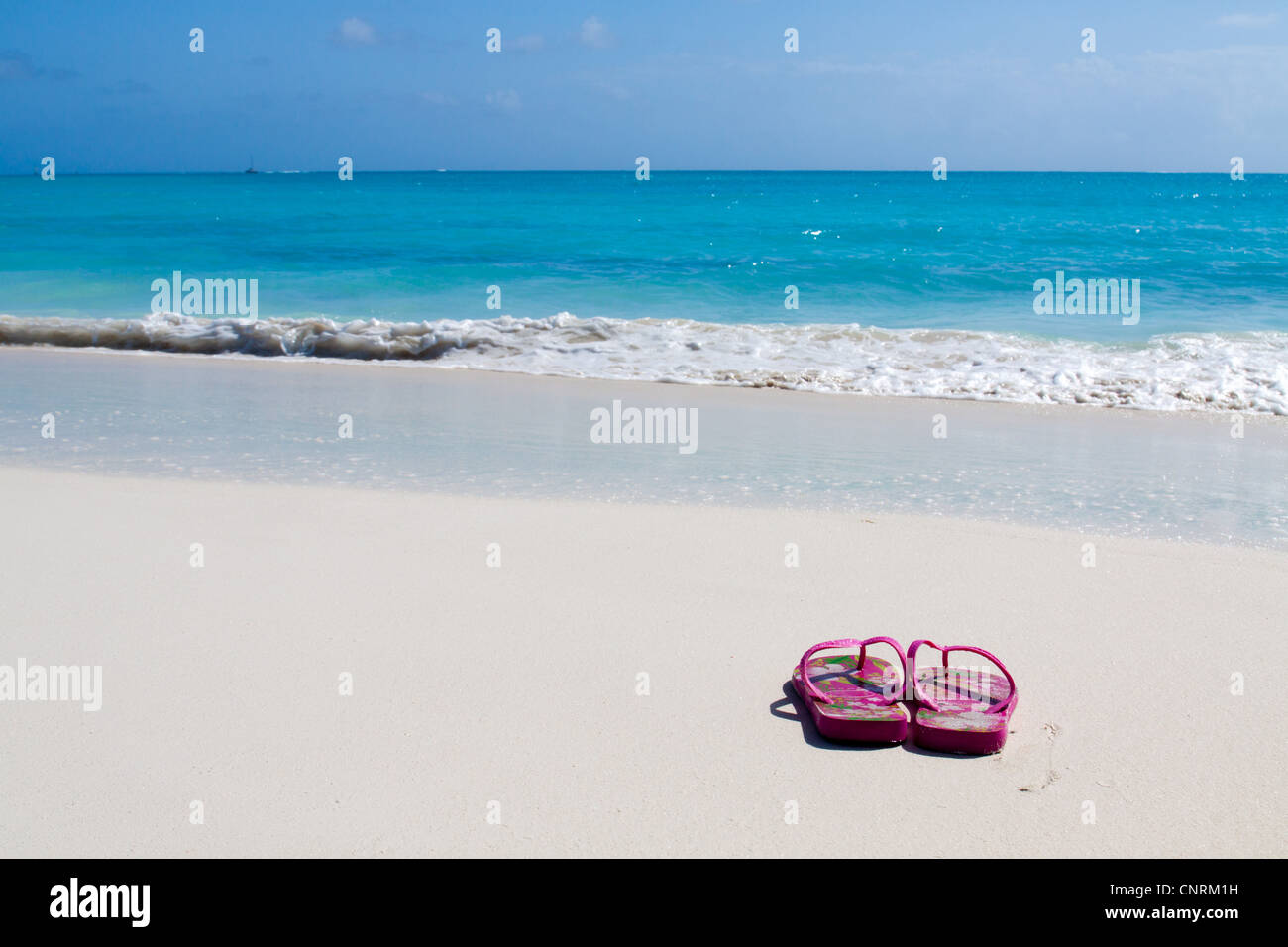 Pair of colored sandals on a white sand beach in front of the sea. The right place for relaxation and vacations Stock Photo