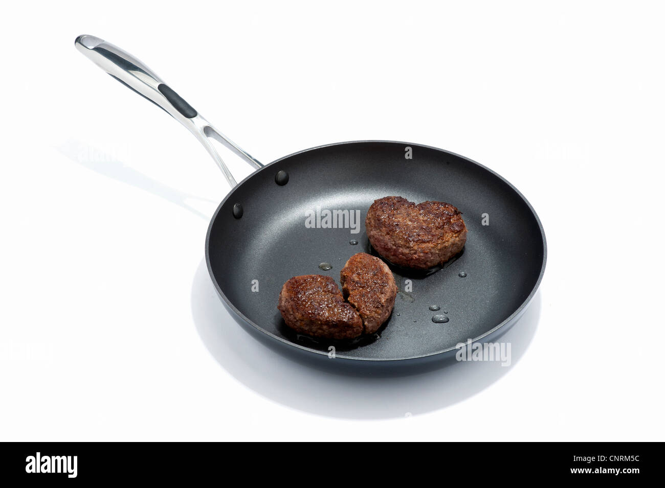 Two heart shaped beef burgers in a frying pan, one broken Stock Photo