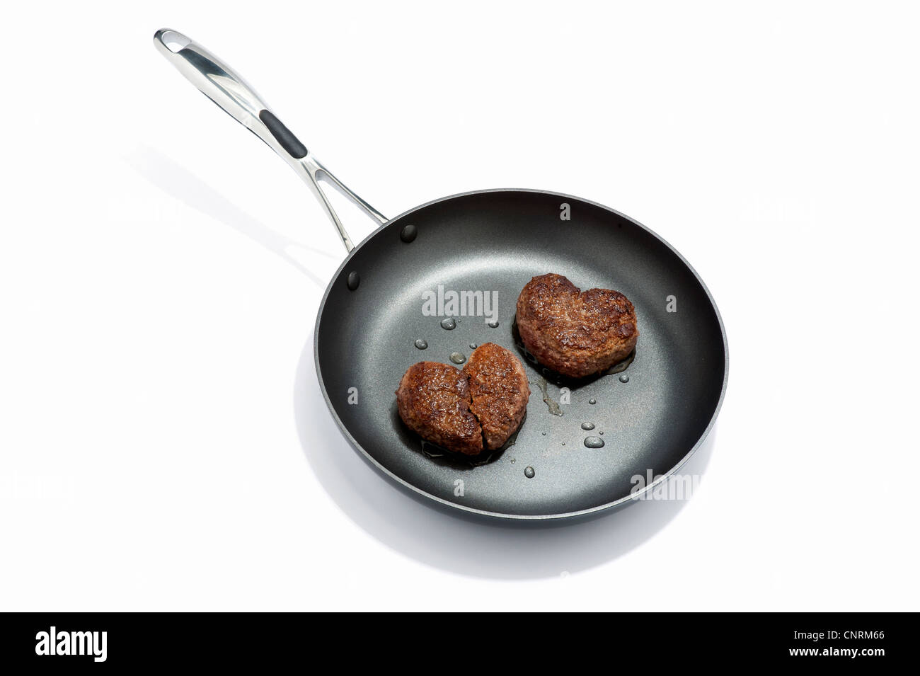 Two heart shaped beef burgers in a frying pan, one broken Stock Photo