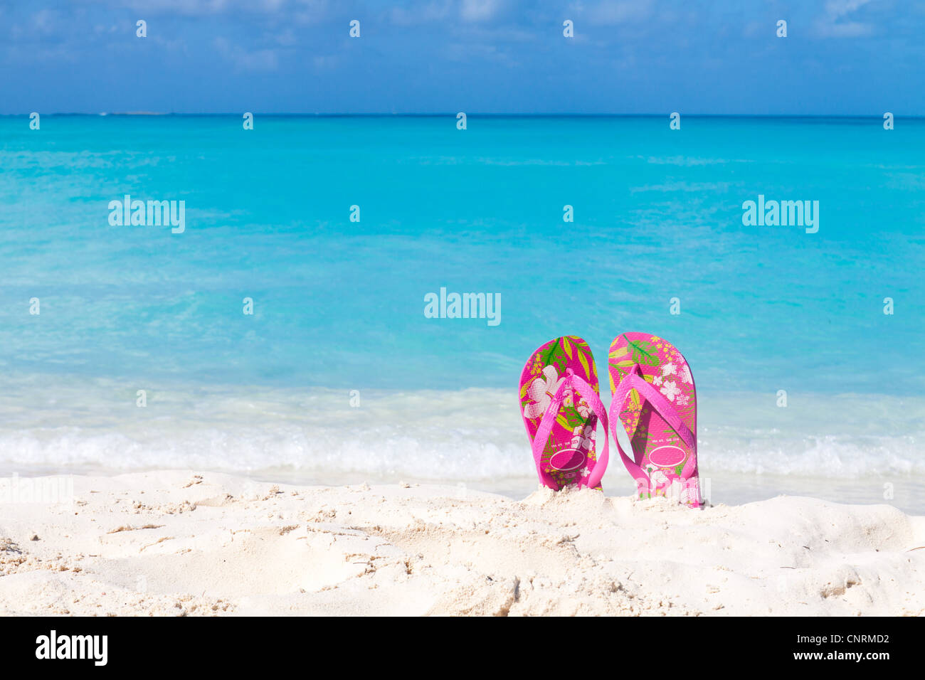 Pair of colored sandals on a white sand beach in front of the sea. The right place for relaxation and vacations Stock Photo