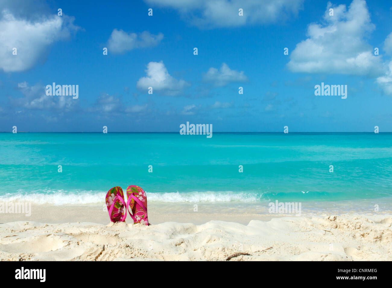 Pair of colored sandals on a white sand beach in front of the sea. The right place for relaxation and vacations Stock Photo