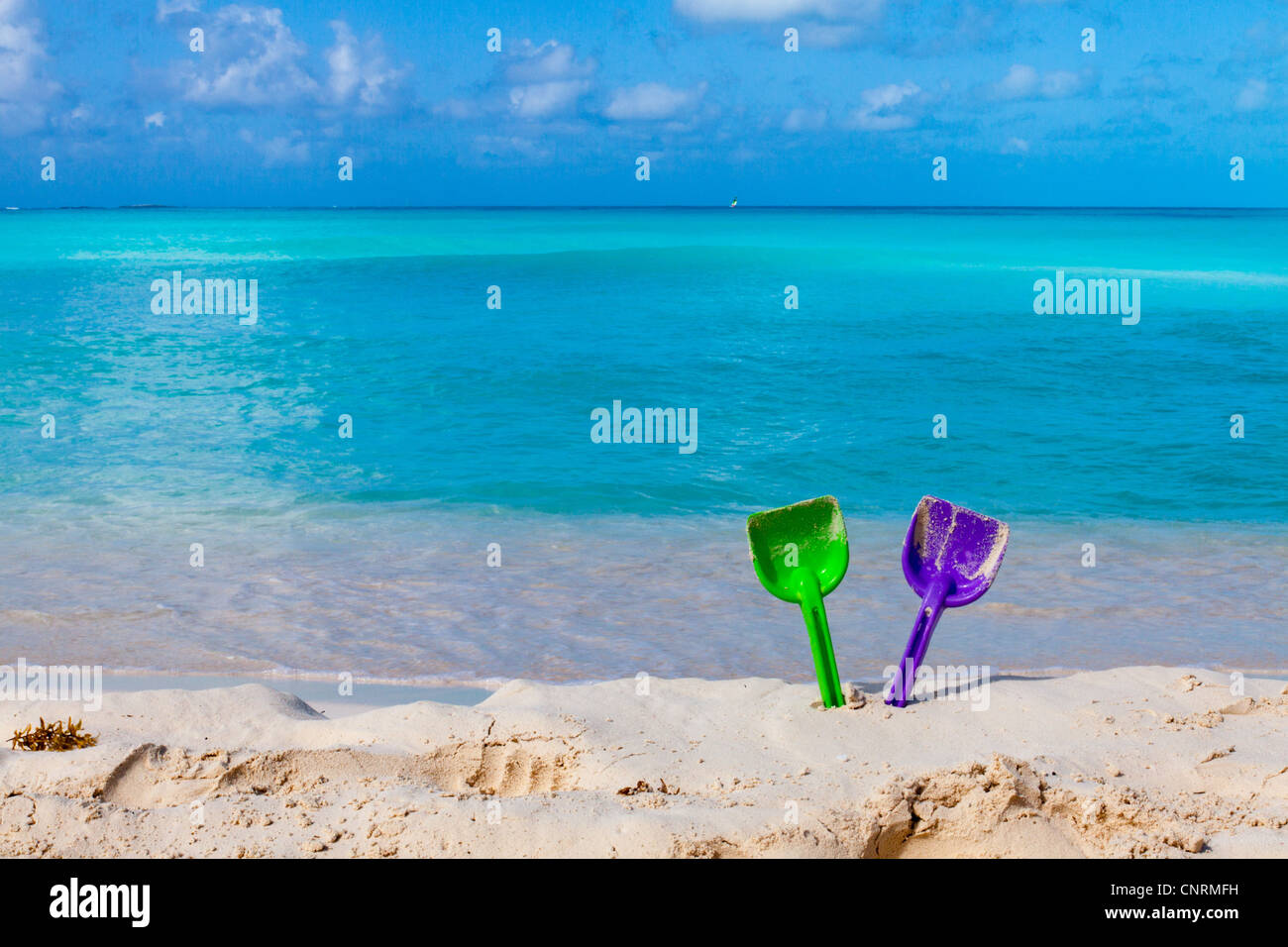 Pair of colored spades on a white sand beach in front of the sea. The right place for relaxation and vacations Stock Photo