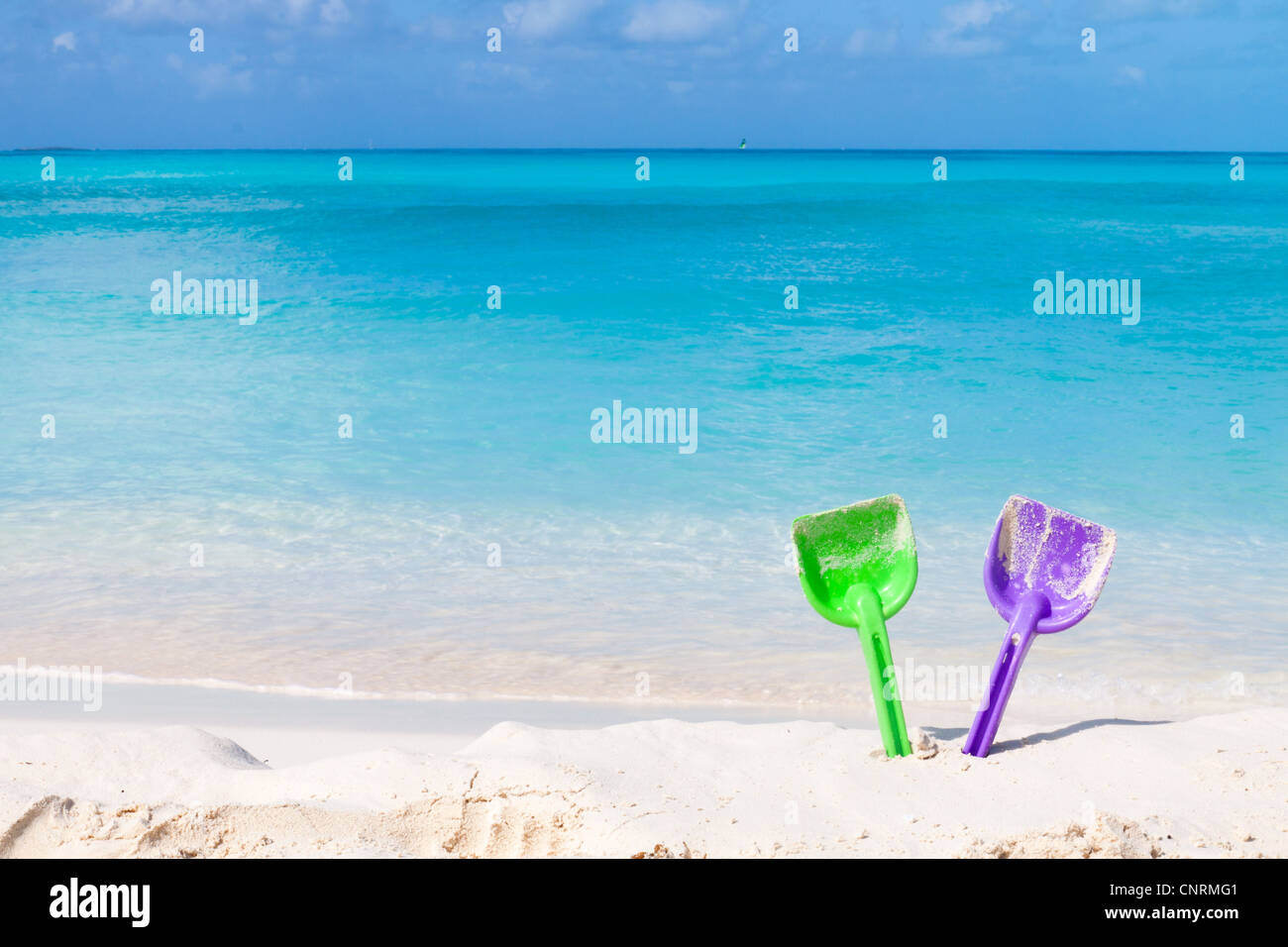 Pair of colored spades on a white sand beach in front of the sea. The right place for relaxation and vacations Stock Photo
