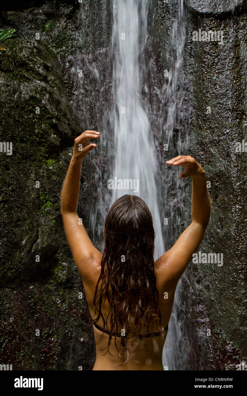 A young woman showers in a natural waterfall in the jungle of Costa