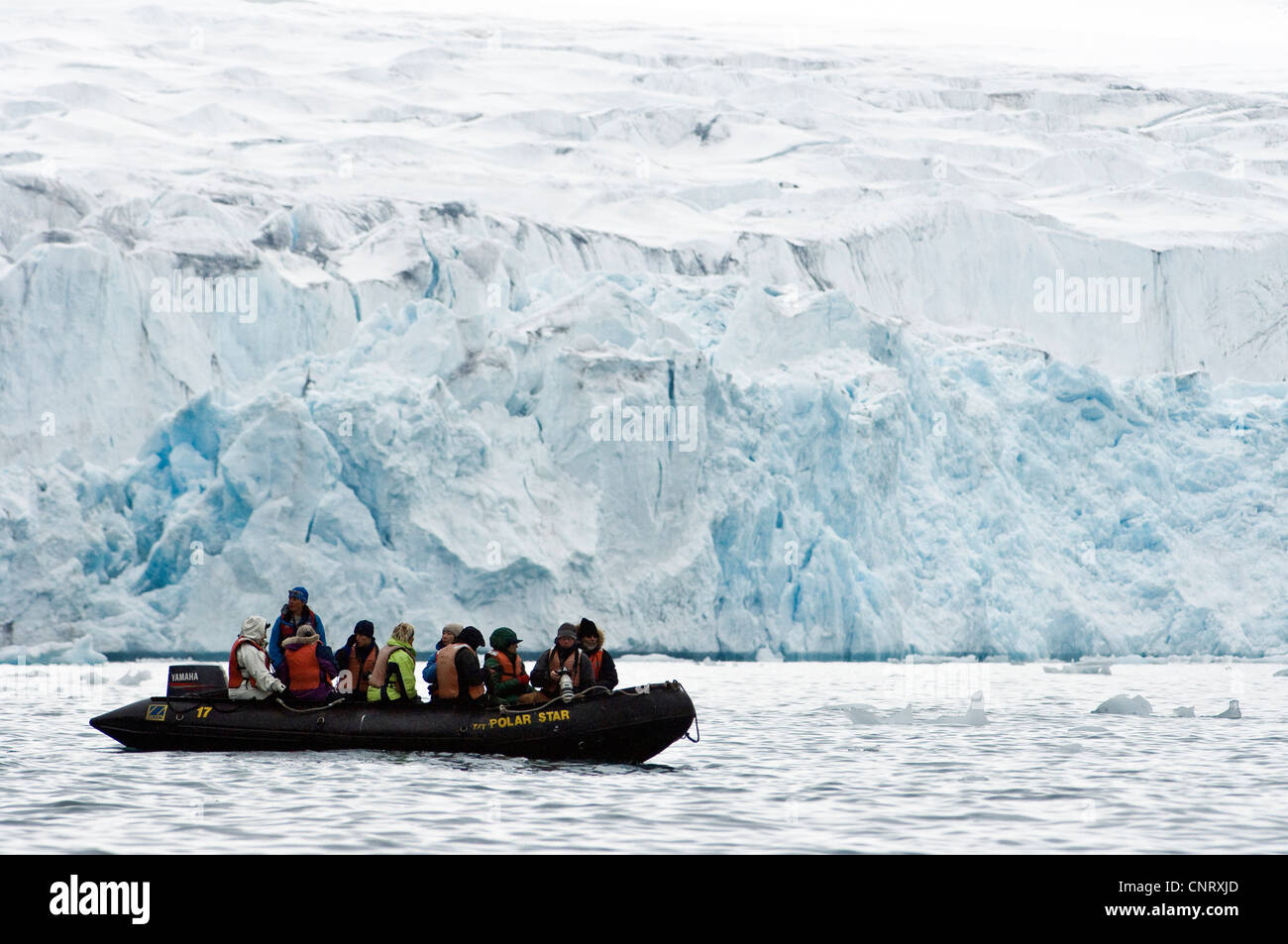 Zodiac with exploration eco-tourists in front of the mighty glacier in Fjortende Julibukta (79 degrees N), Norway, Svalbard, Svalbard Inseln Stock Photo