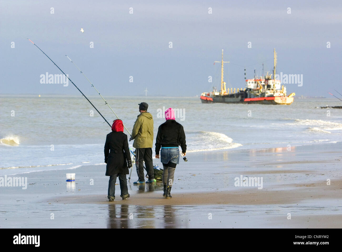 angler and walker at the beach, ship in background, Netherlands, Zeeland, Breskens Stock Photo