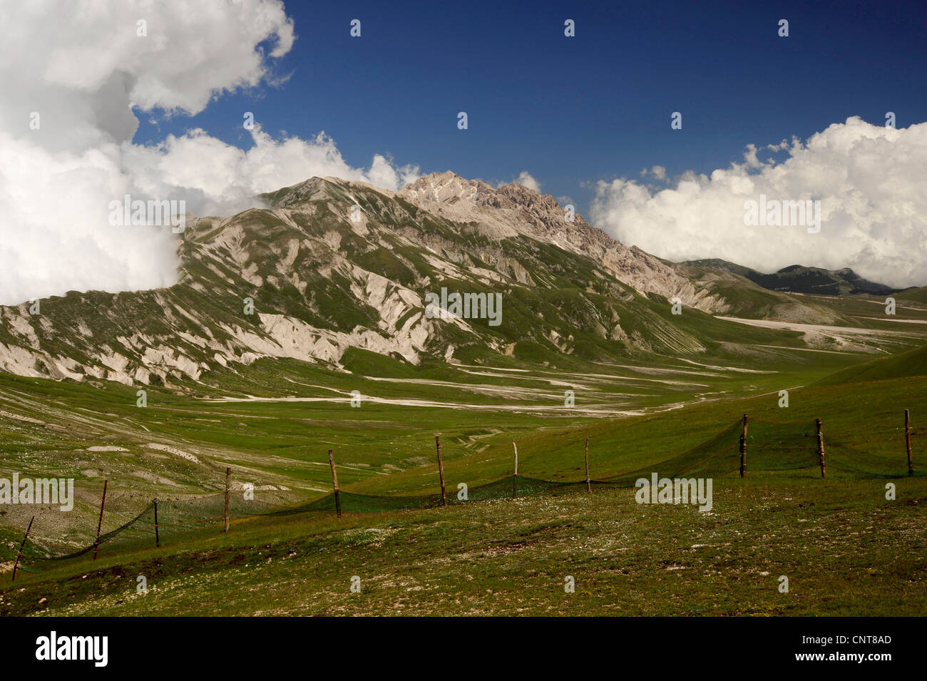 mountain pasture fenced in on extensive dry meadow plains in front of a mountain range, Italy, Nationalpark Abruzzen Stock Photo
