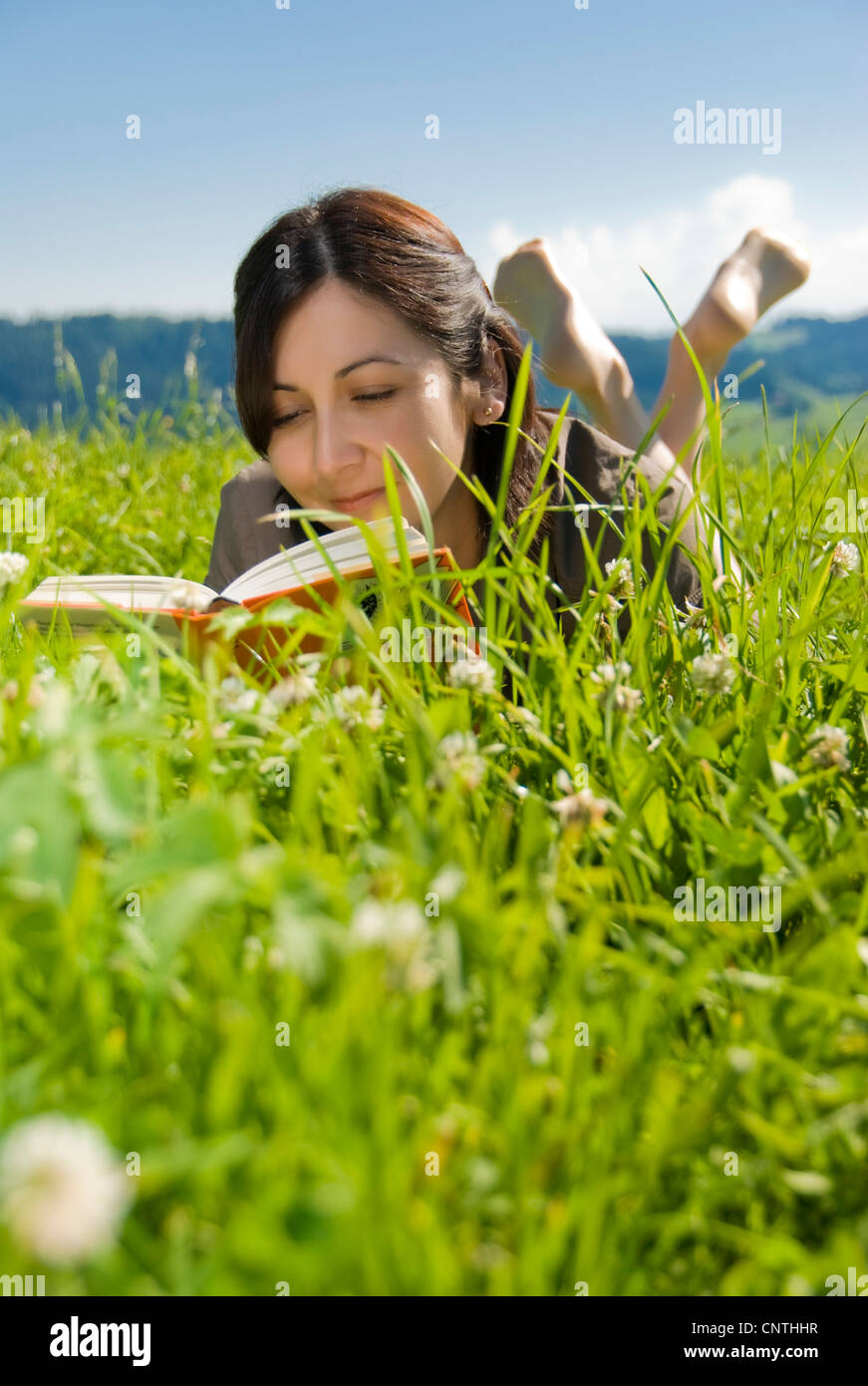 young woman lying in a meadow reading a book Stock Photo