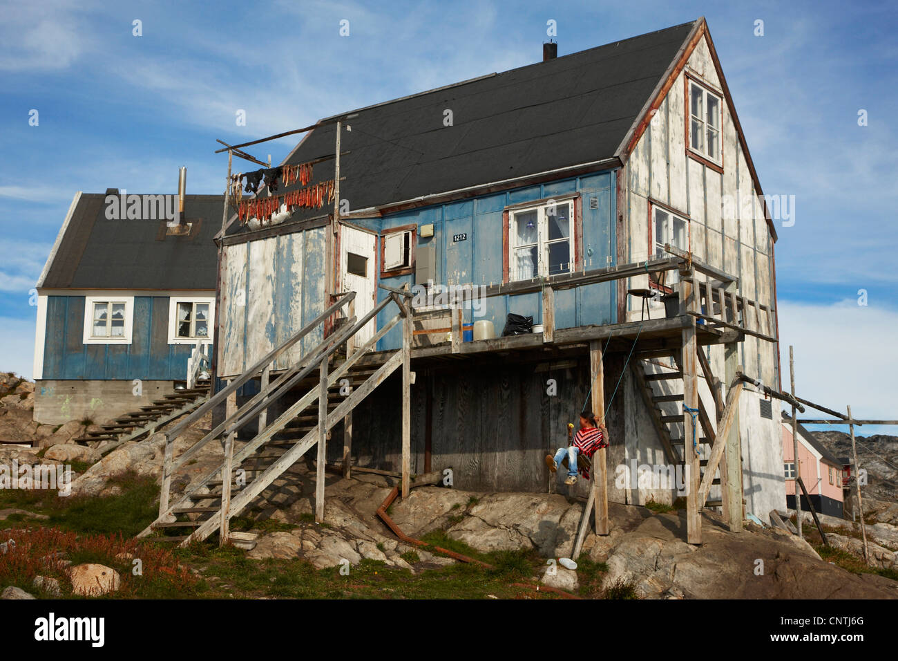 girl seesawing at wooden house, Greenland, Ammassalik, East Greenland, Tiniteqilaq Stock Photo