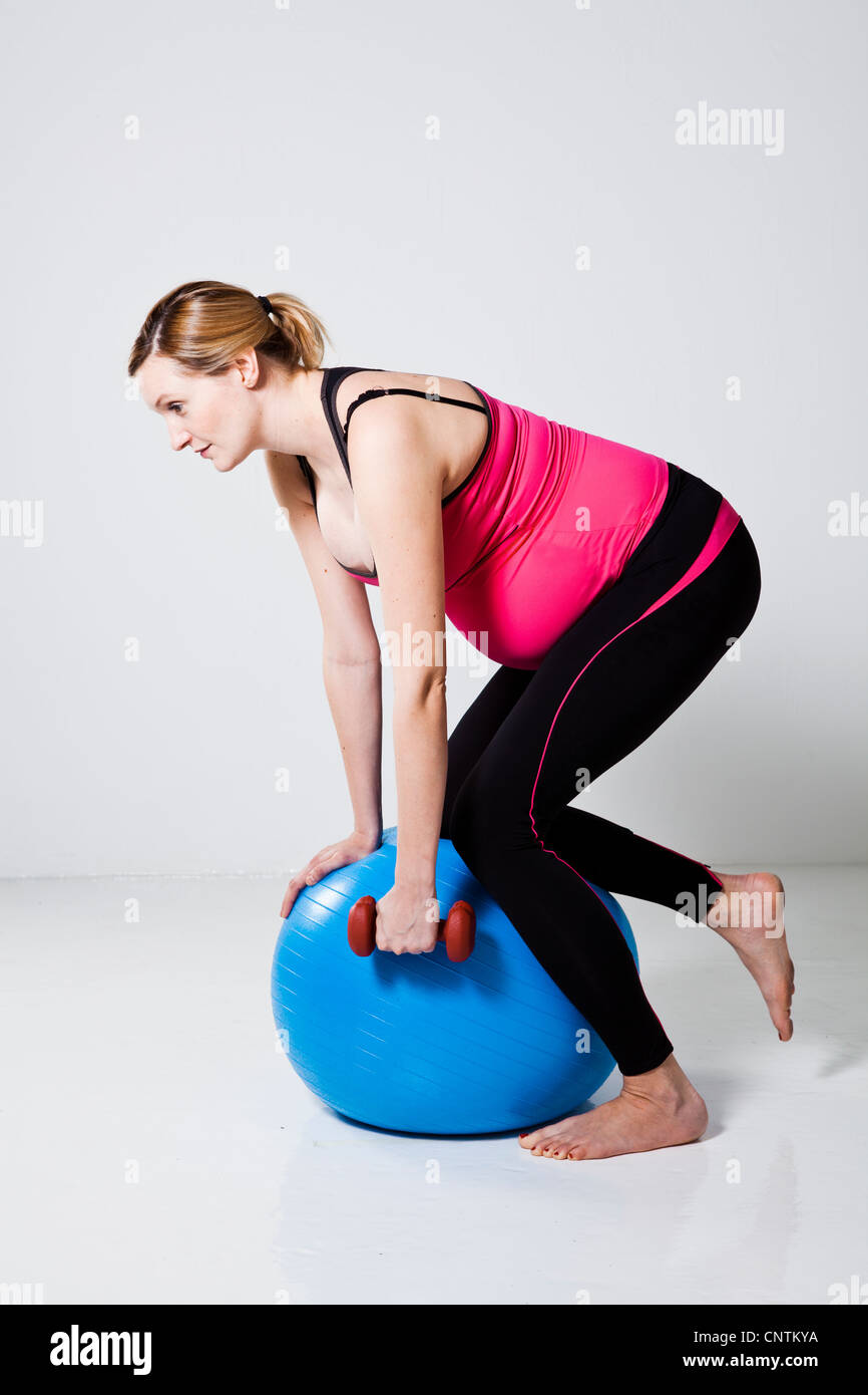 Pregnant woman doing a rowing exercise with dumbbells while kneeling on