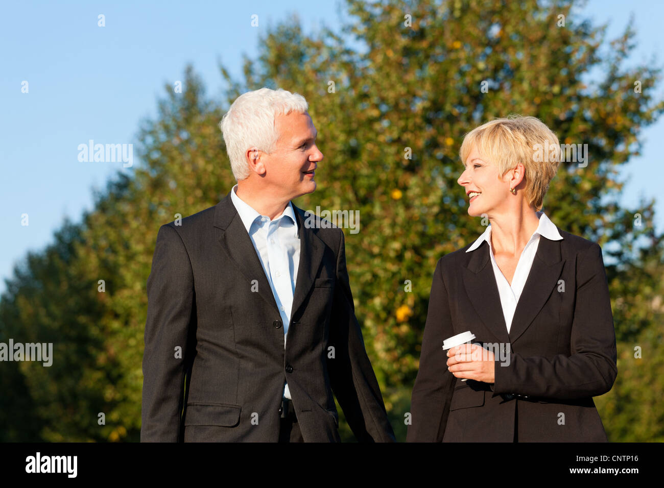 Business people - mature or senior - talking outdoors and walking in a park Stock Photo