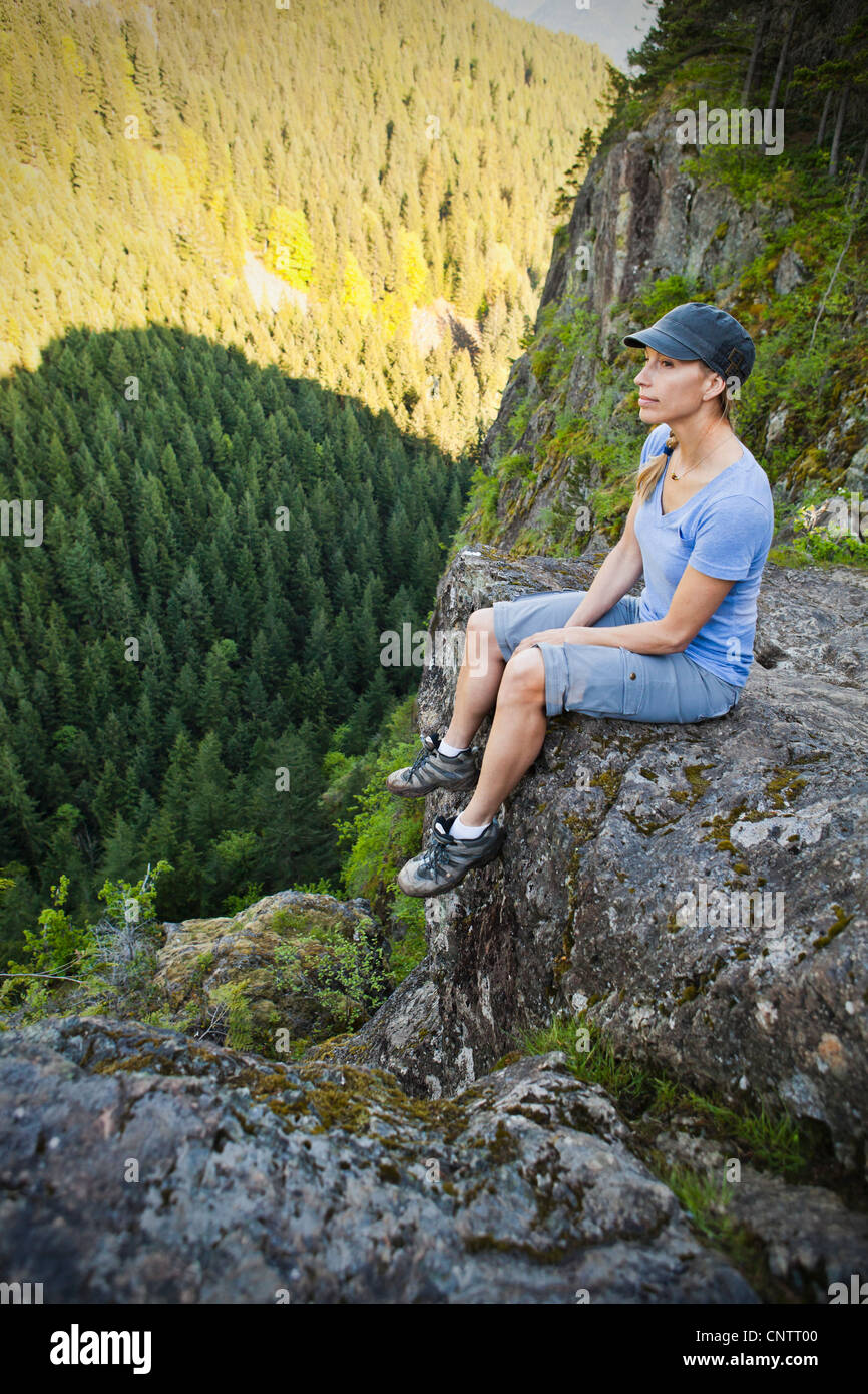 A woman hiker sitting on the edge of a rocky cliff looking up at a ...
