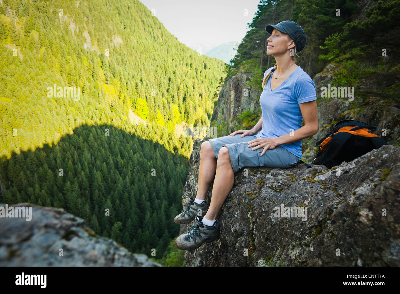 A woman hiker sitting on the edge of a rocky cliff with eyes closed in ...