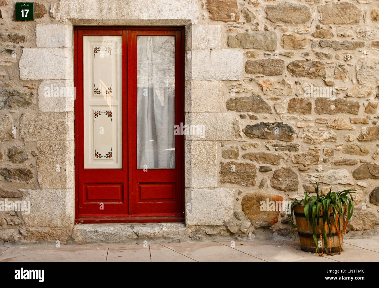 a red door in a stone house, wall and a flowerpot Stock Photo