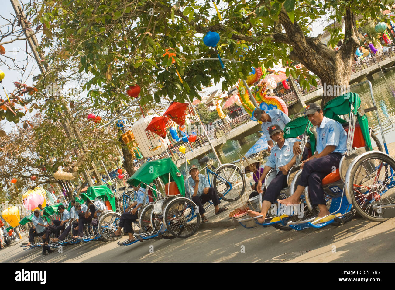 Horizontal view of cycle-rickshaws or cyclos and drivers waiting for customers in the ancient town of Hoi An, Vietnam on a sunny day. Stock Photo