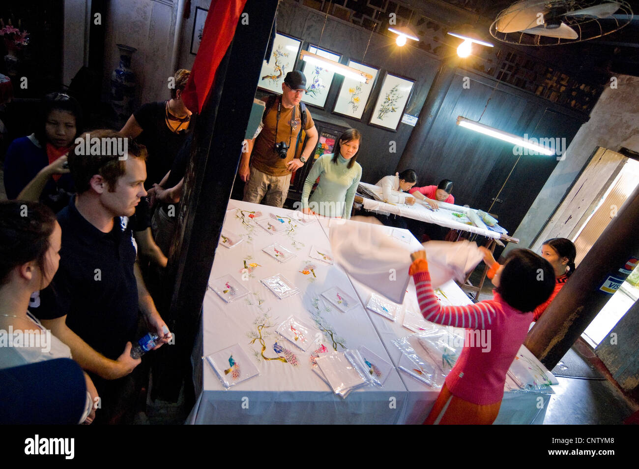 Horizontal interior aerial view of ladies selling their embroidered table linen to a group of Western tourists. Stock Photo